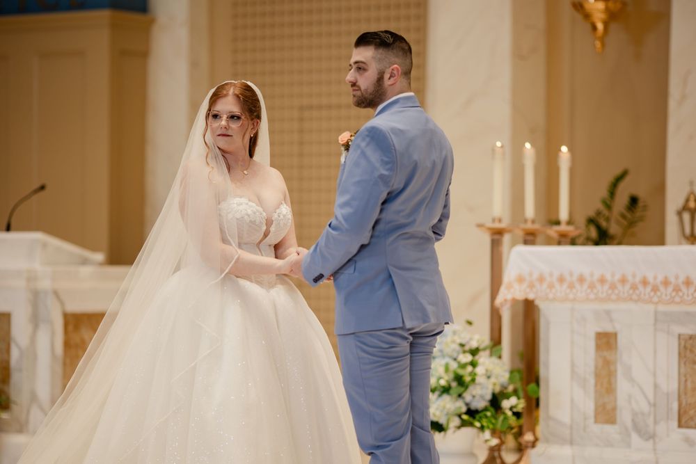 A couple exchanges vows during their wedding ceremony in an elegant church with glowing candles in the background.