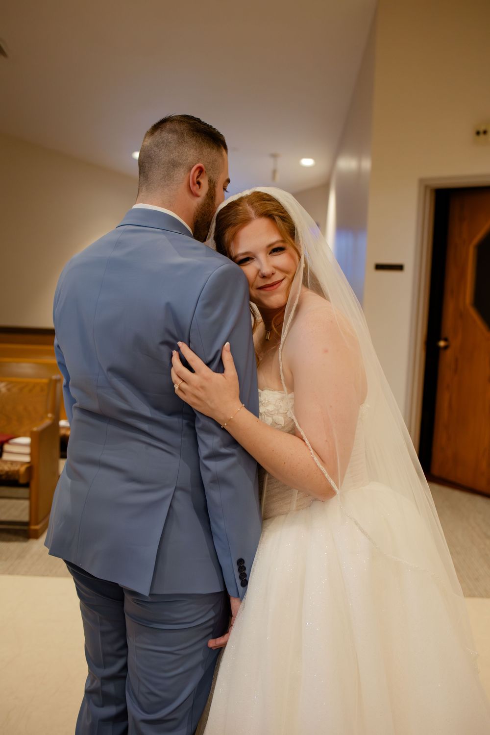 A romantic moment between newlyweds as the bride in a flowing white dress smiles while embracing her groom in a blue suit.