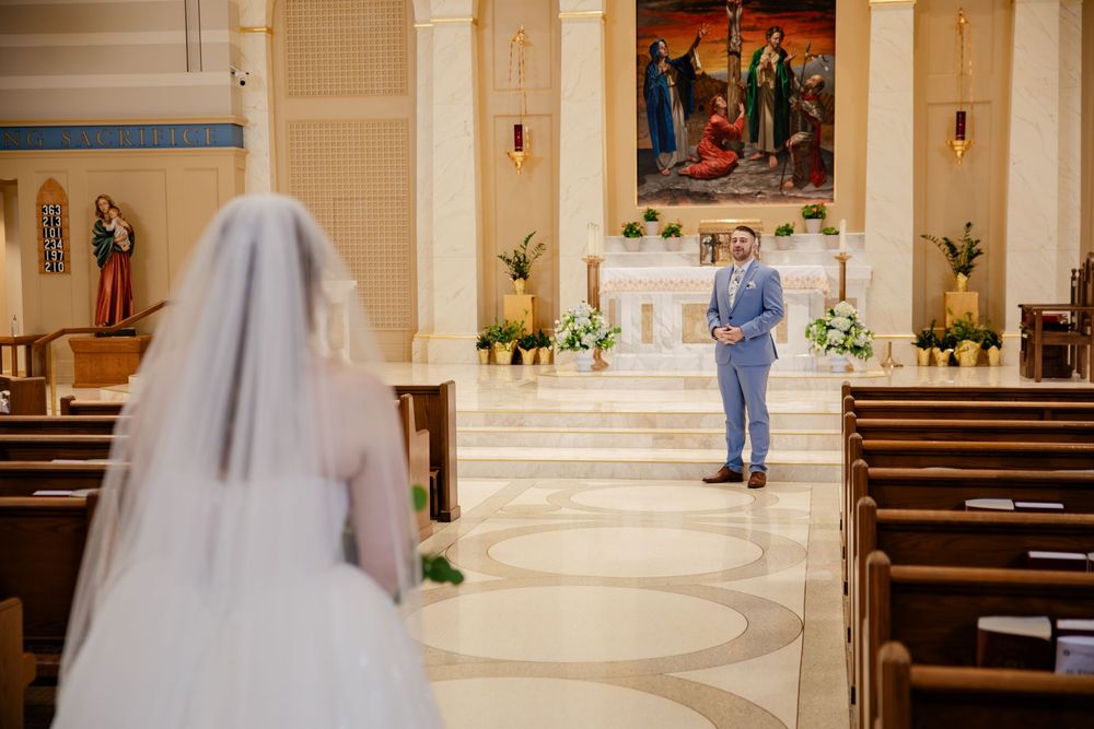 A bride in a traditional white wedding dress and veil walks down the aisle of a church decorated with flowers.