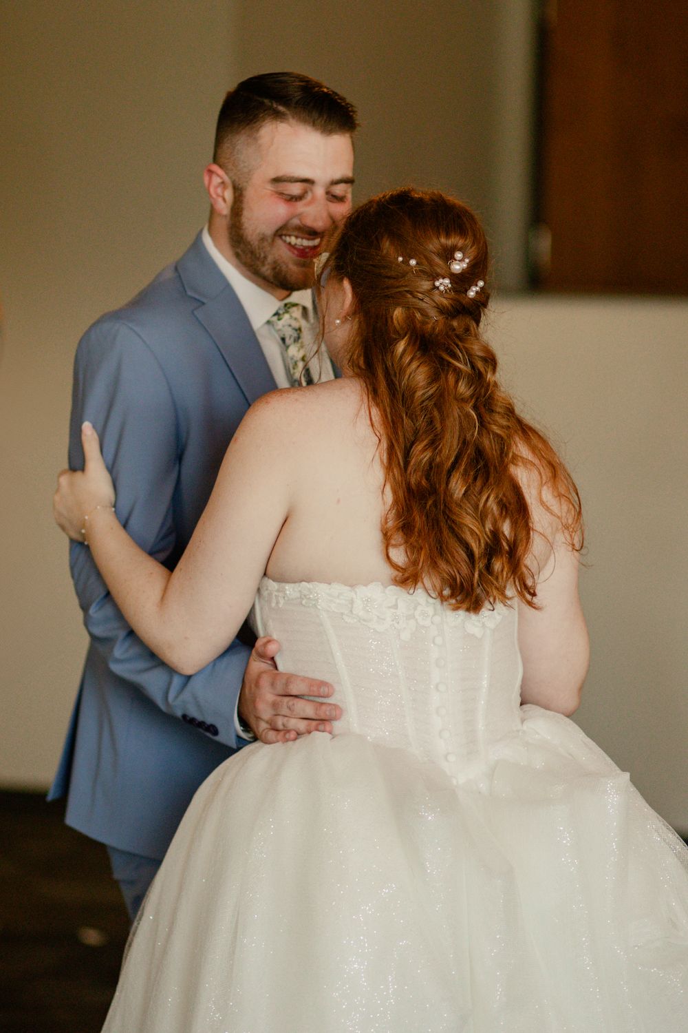 A tender moment between newlyweds as they share their first dance, with the bride's lace gown and intricate hair details visible.