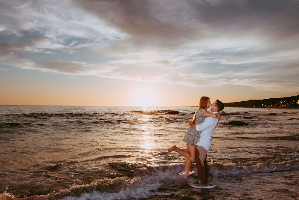 Loving couple shares romantic moment at sunset on tropical beach with golden sun glinting off ocean waves in Newport Beach.