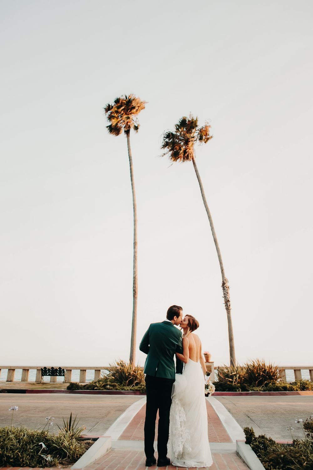 A romantic wedding couple shares intimate photos against a palm tree backdrop at sunset in Orange County, California.