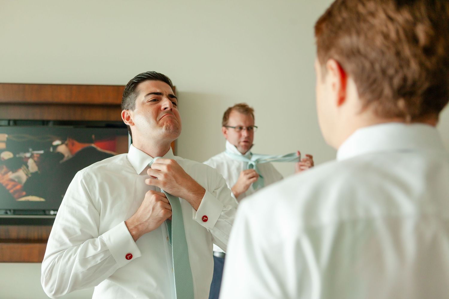 Groomsmen helping each other with mint green ties while getting ready for the wedding ceremony.