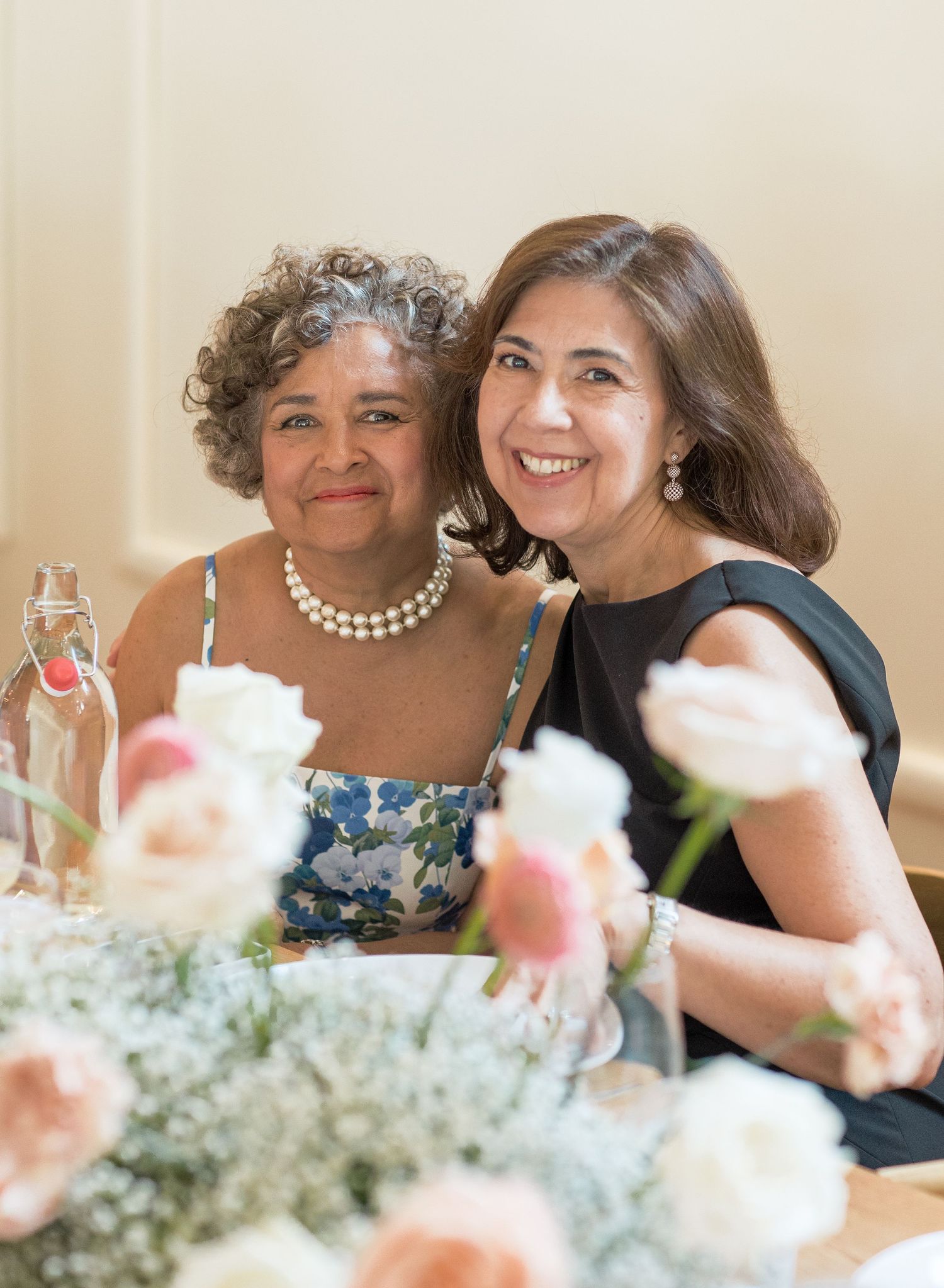 People sharing joyful moments during a celebration with pink flowers and delicate table decor in view.