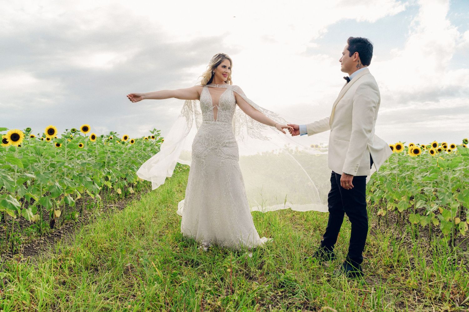 Couple holding hands in sunflower field during romantic wedding photoshoot.