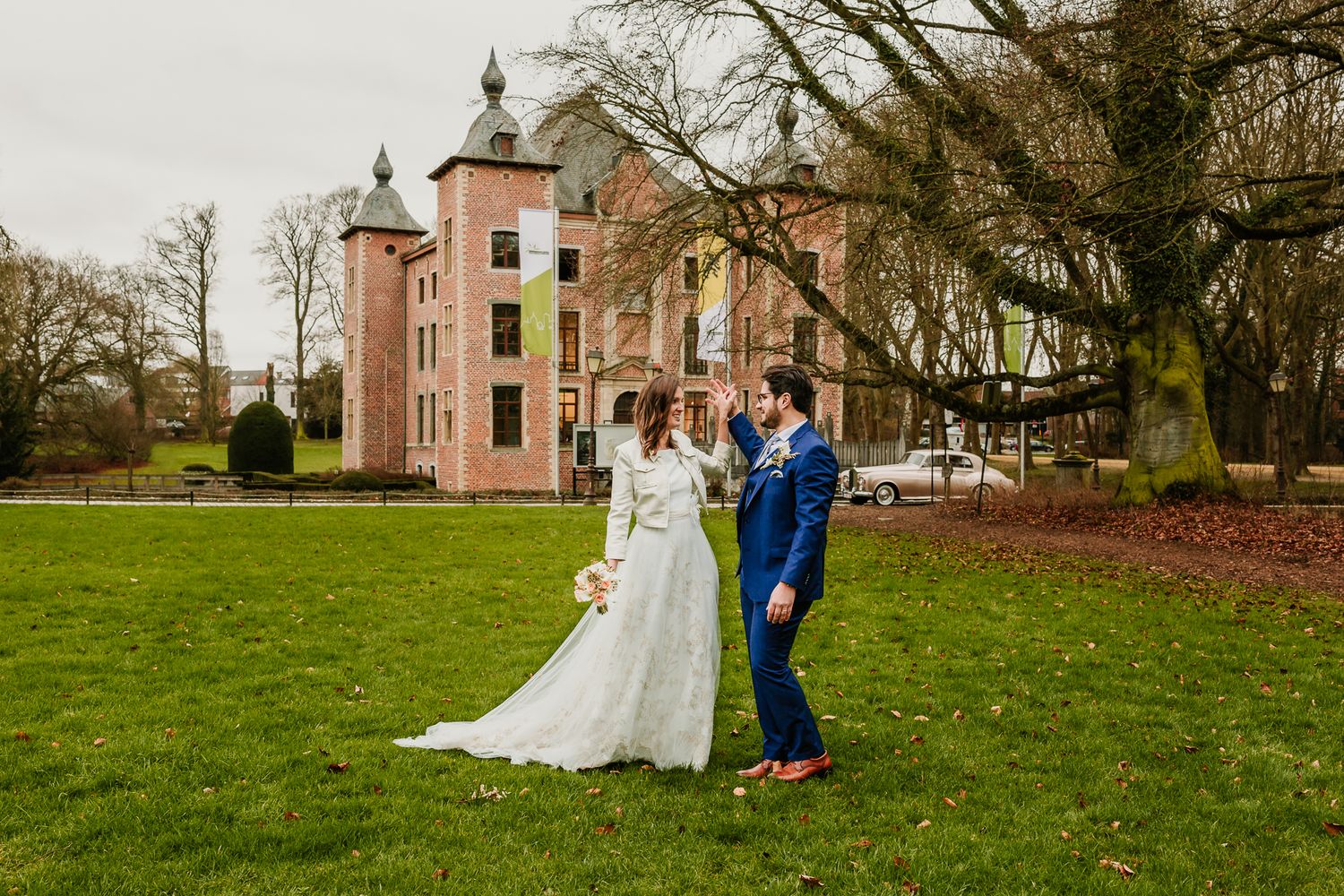 Wedding party enjoys outdoor portraits on the lawn of a historic estate with a pink stone mansion on a fall afternoon.