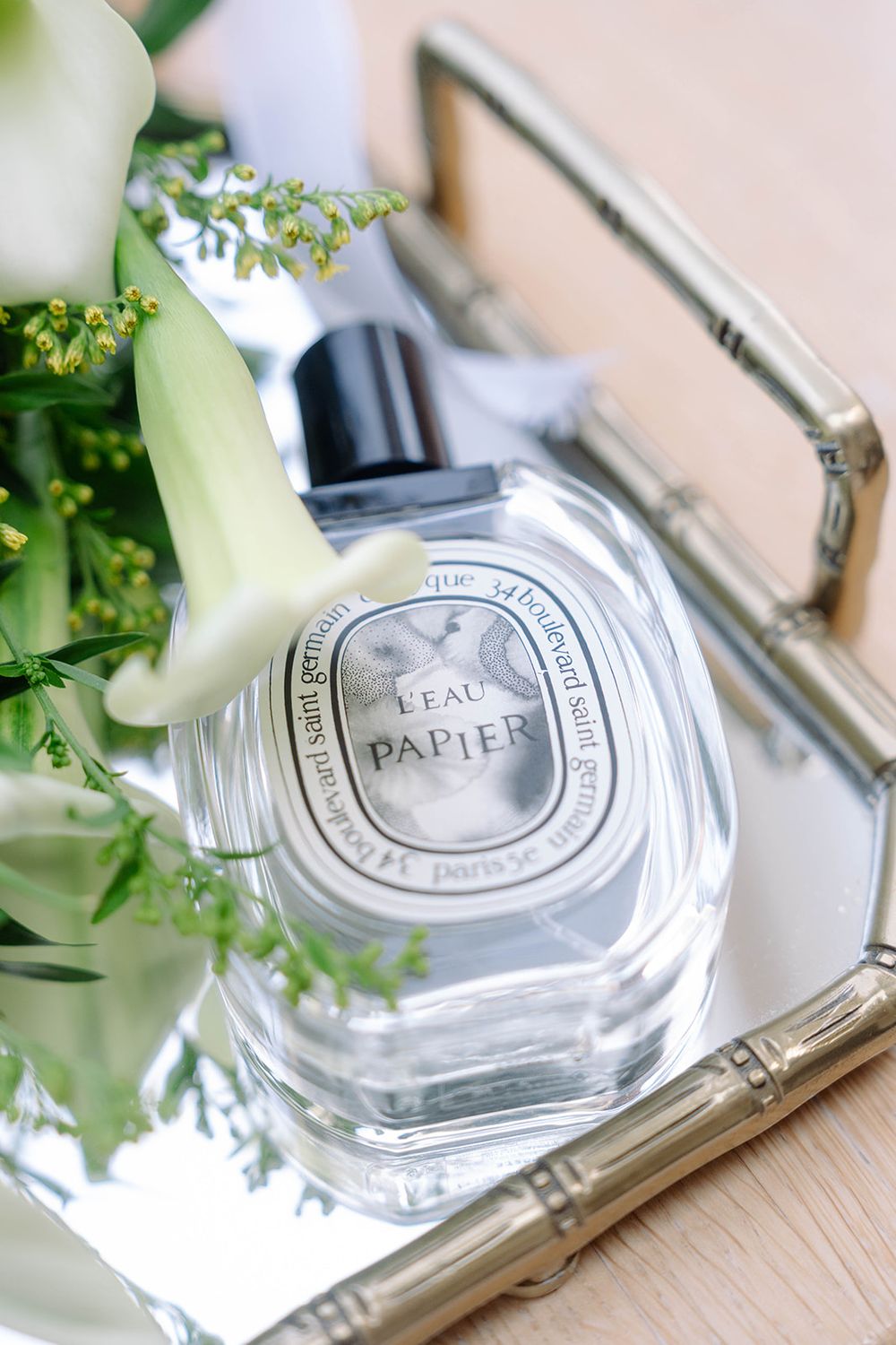 Diptyque perfume bottle on a mirrored tray with elegant floral arrangements.
