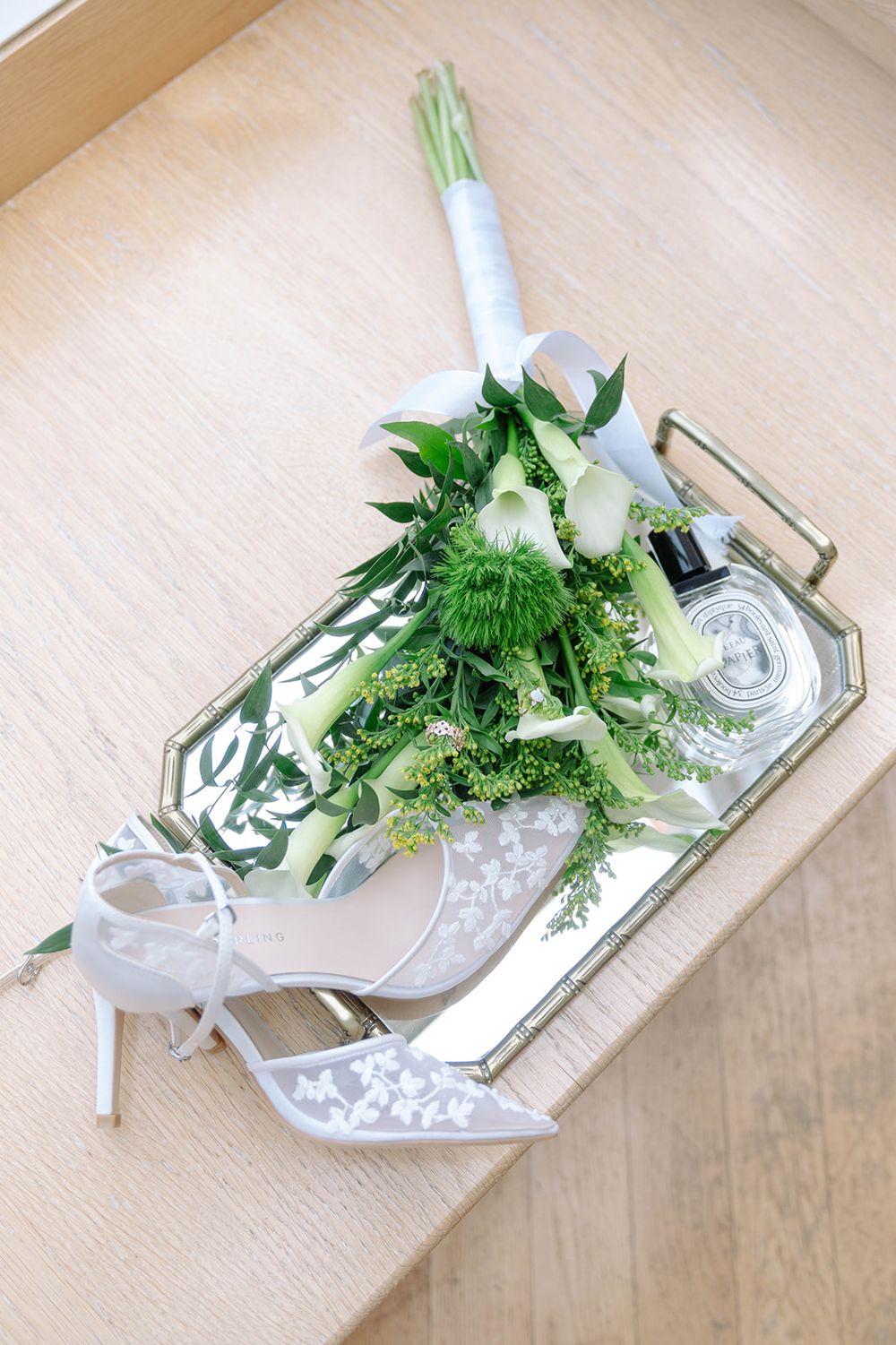 White bridal bouquet and elegant heels arranged on a mirrored silver tray.