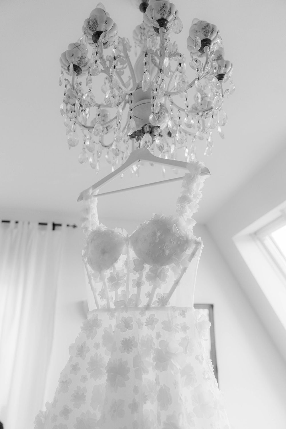 Black and white photo of a wedding dress suspended under an ornate crystal chandelier.