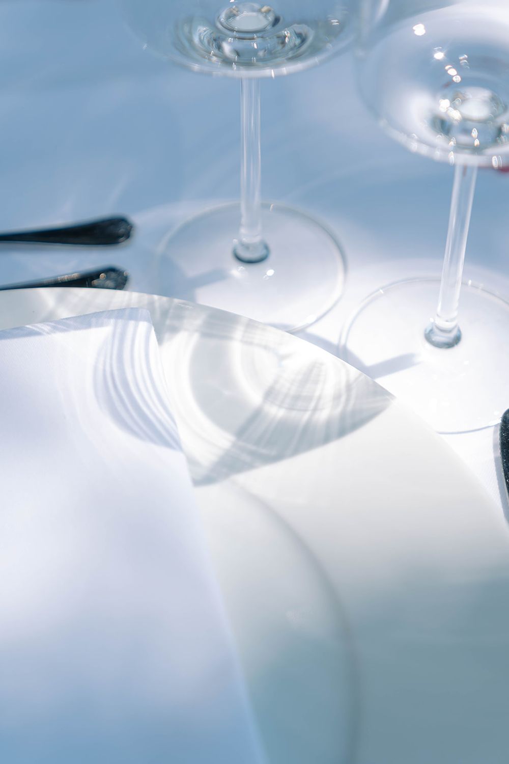 Close-up of wine glass stems on a white tablecloth with soft lighting.