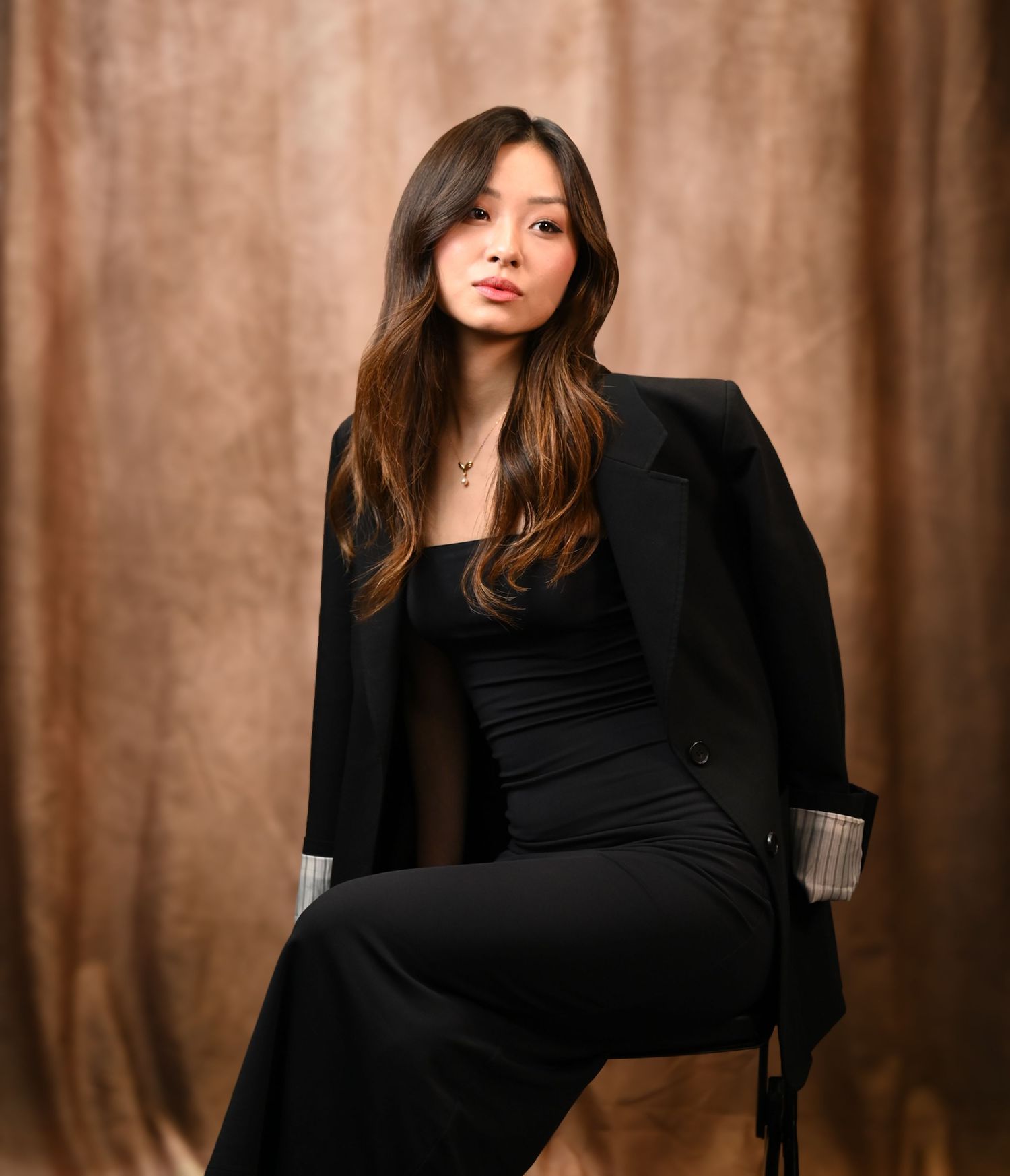 Woman in black attire poses gracefully against textured brown backdrop in elegant portrait series.
