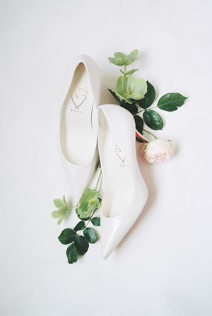 White bridal ballet flats with delicate green foliage accents arranged on a light background.
