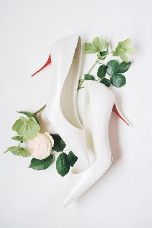Minimalist flat lay composition with elegant white stiletto heels and scattered green leaves on light background.