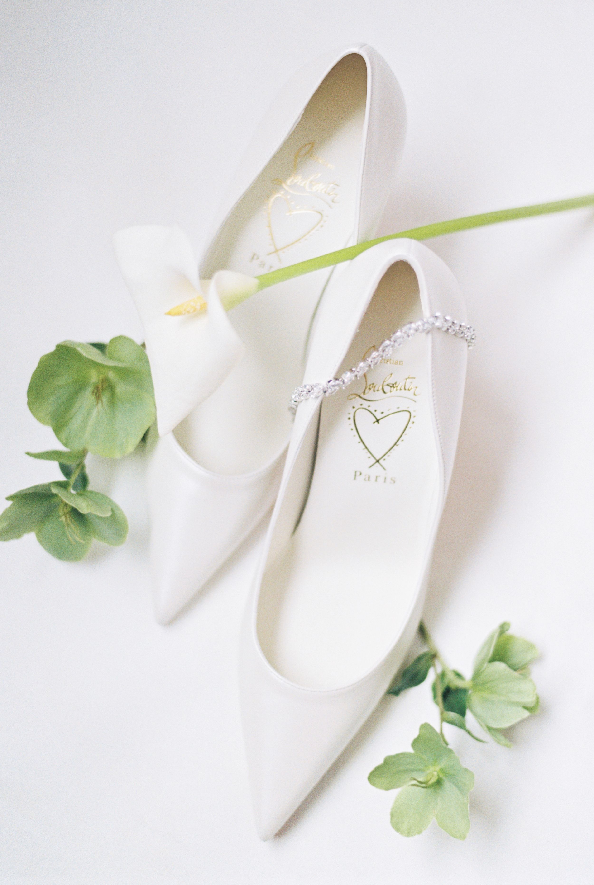 Elegant white bridal shoes with delicate leaves and floral elements on a light background.