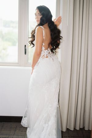 Elegant lace wedding dress captured in a bright window-lit room showing delicate details and flowing train.