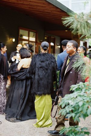 Wedding guests gather outside a venue wearing formal attire including black suits and elegant dresses.