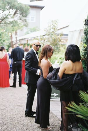 Wedding guests in formal black attire mingle during an outdoor cocktail reception.