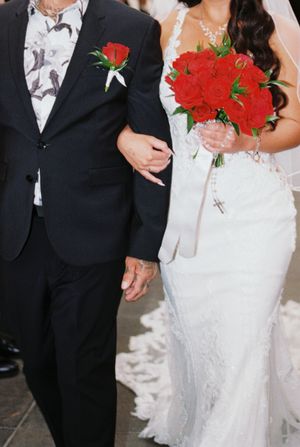 Wedding couple poses with vibrant red rose bouquets against elegant formal attire.