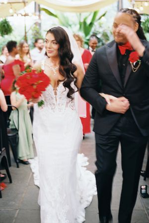 A wedding couple walks together at their celebration with the bride holding a vibrant red bouquet.