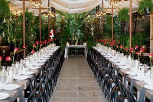 Long reception tables set with black chairs and white linens in an elegant greenhouse-style venue.