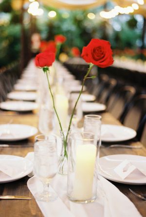 Simple white candlelit table setting with red roses in glass bud vases create an elegant romantic dining atmosphere.