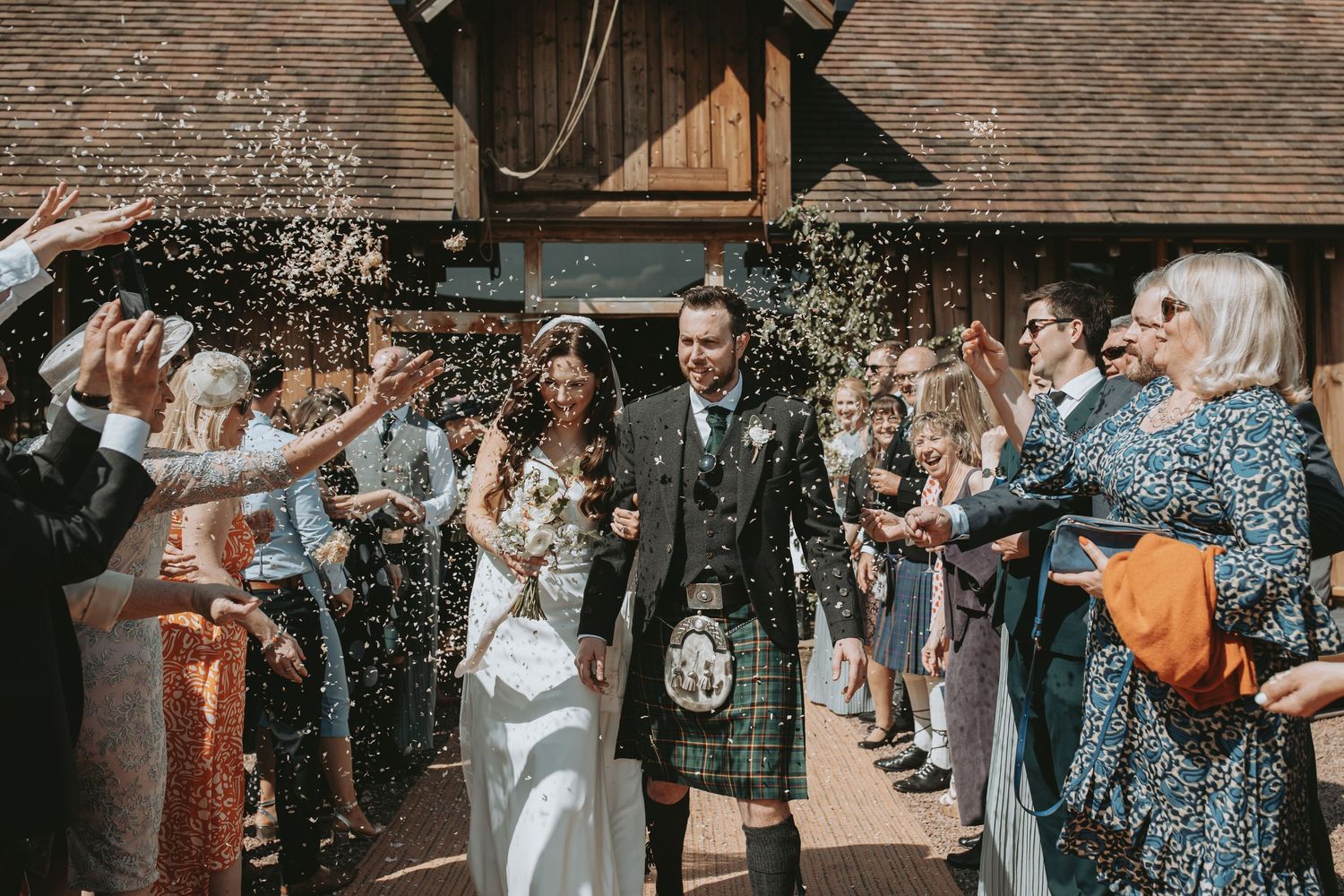 Wedding guests shower the happy couple with natural flower confetti in a joyful outdoor celebration.
