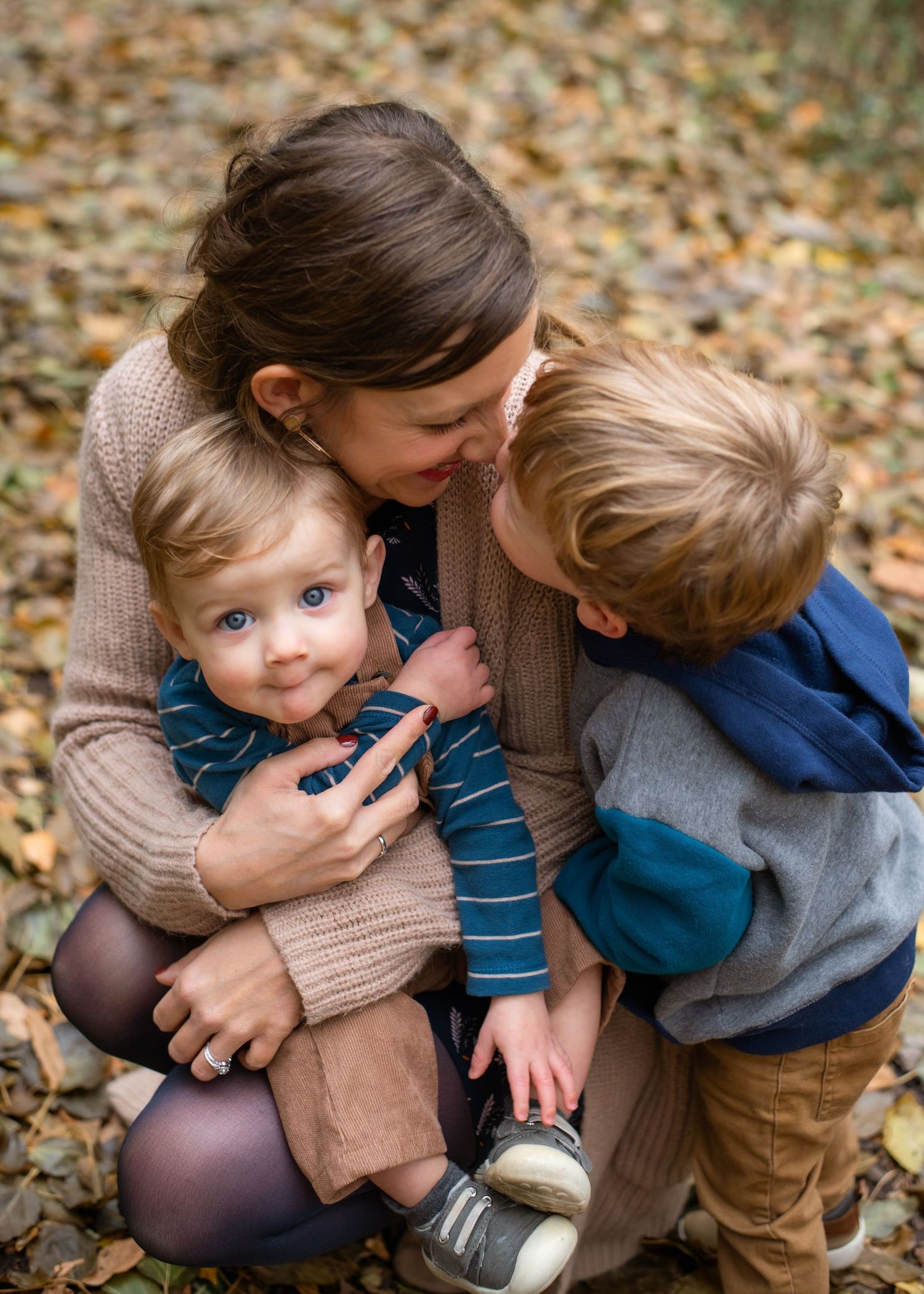 A child and parent share a playful moment together in a pile of fallen autumn leaves.
