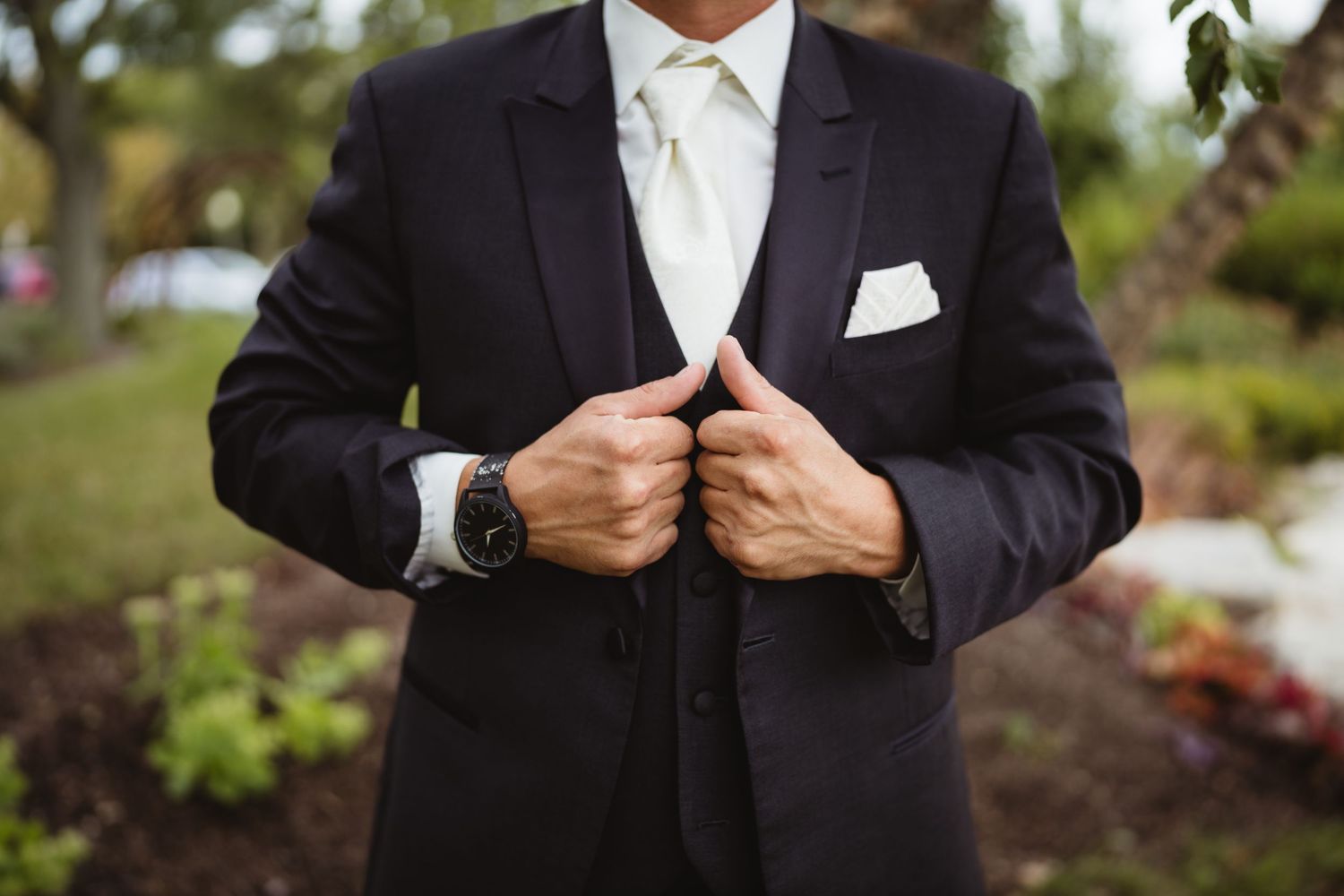 Smart black tuxedo suit with crisp white shirt and pocket square photographed outdoors in a garden setting.