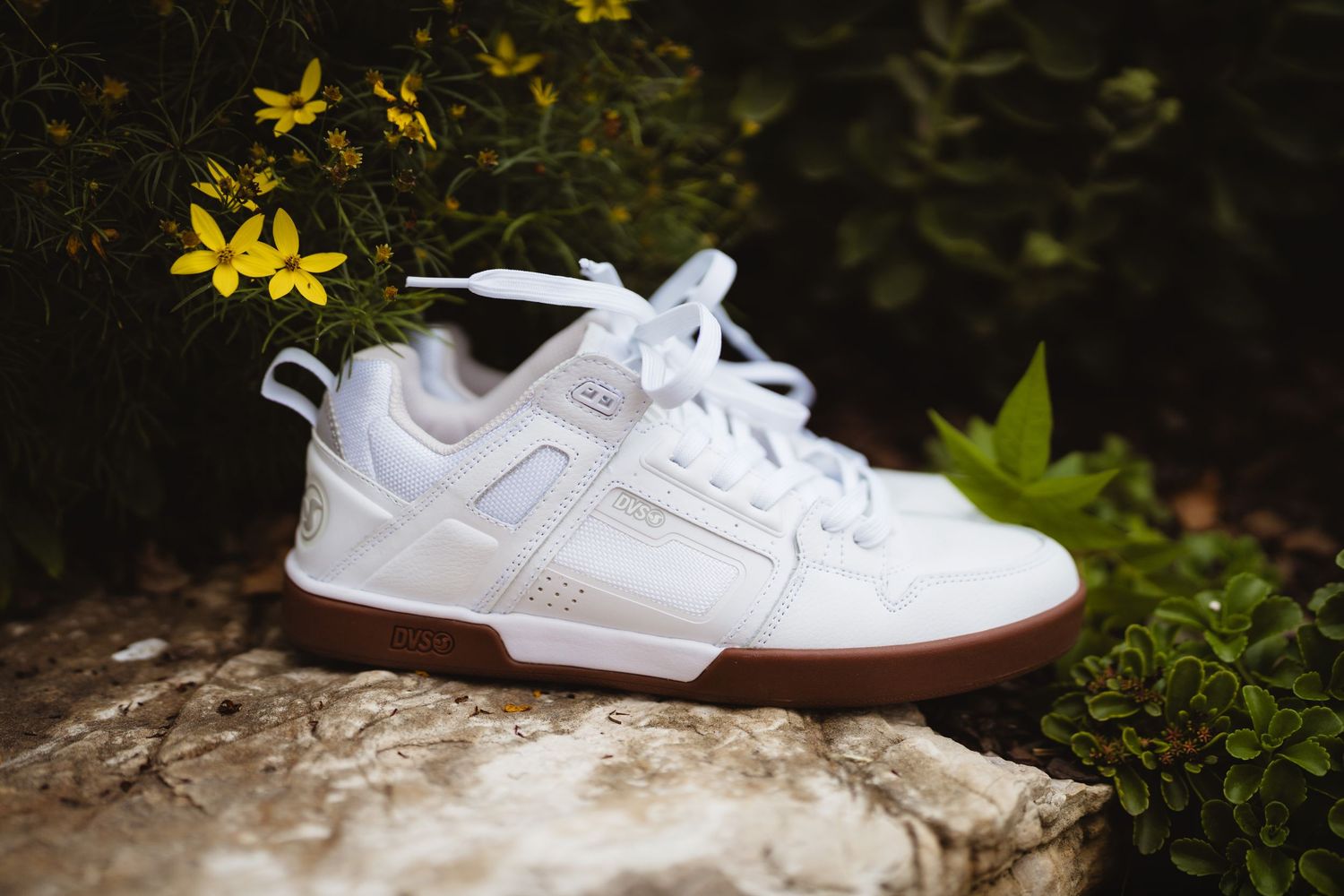 White DC sneakers sitting on mossy ground with yellow flowers in the background.