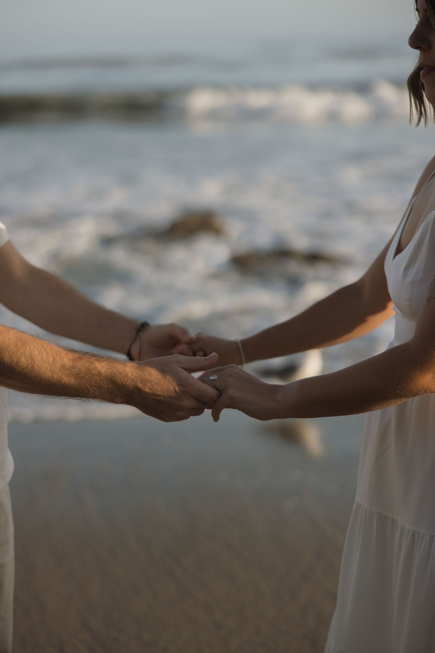 Close-up engagement photo of couple holding hands at El Matador Beach in Malibu