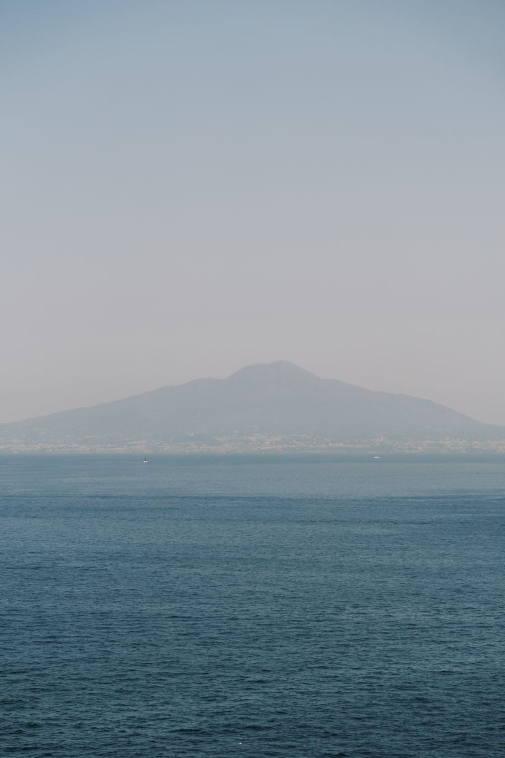 Tranquil seascape with distant mountain silhouettes and calm blue waters under a hazy sky.
