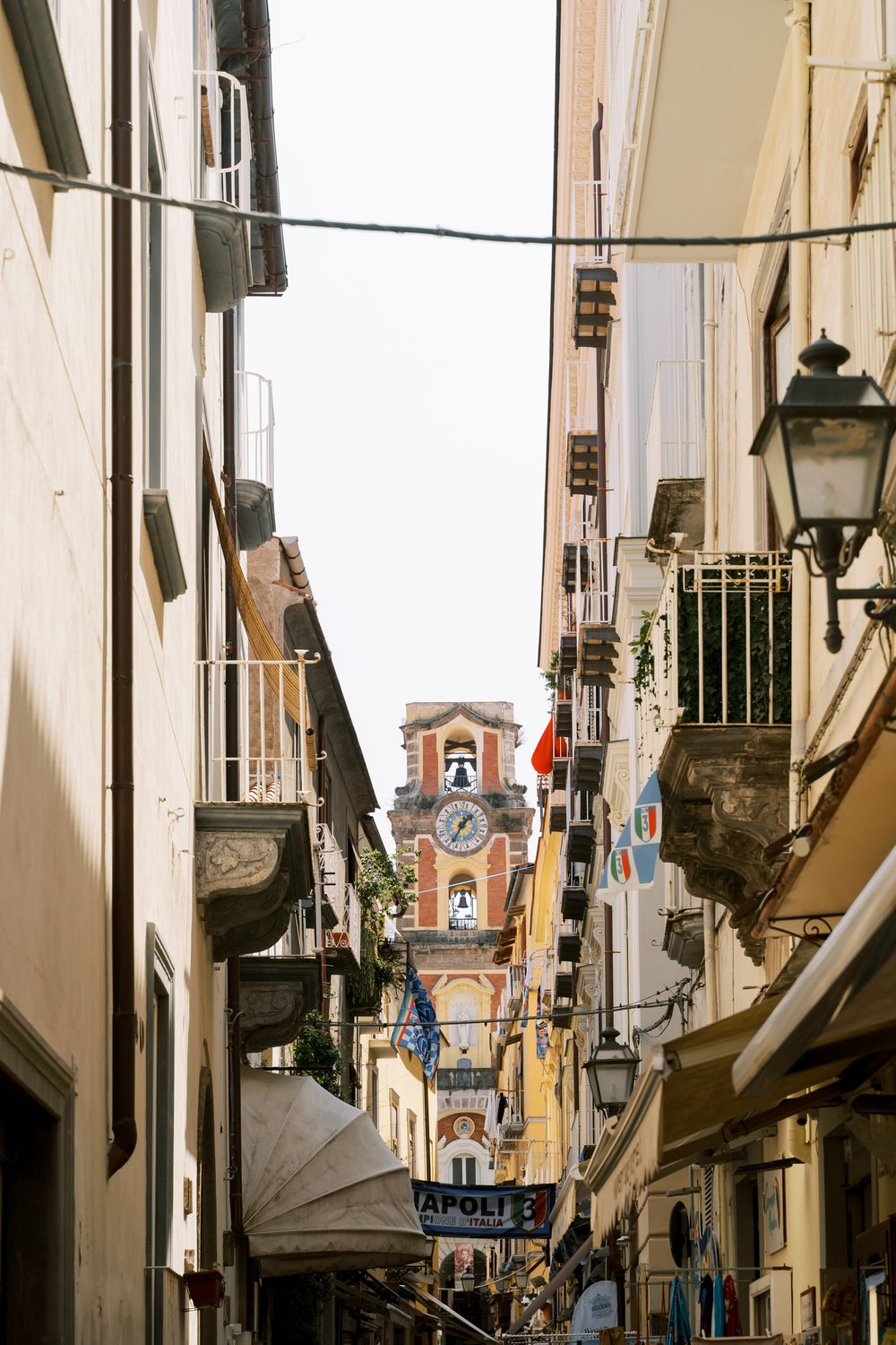 Narrow cobblestone street in Portugal with traditional architecture and a church bell tower visible in the distance.
