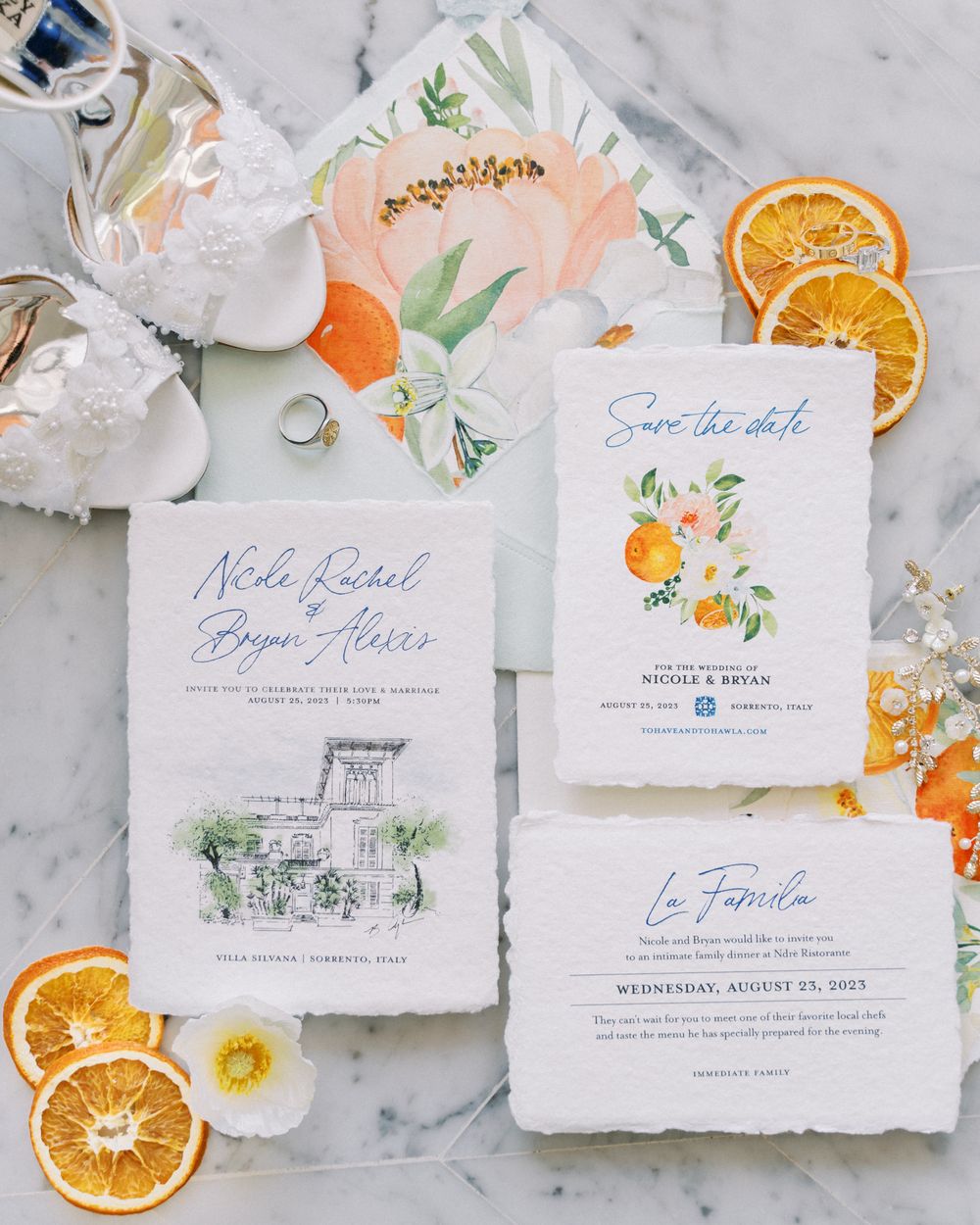 Elegant wedding invitation suite with orange slices and floral accents on marble background.