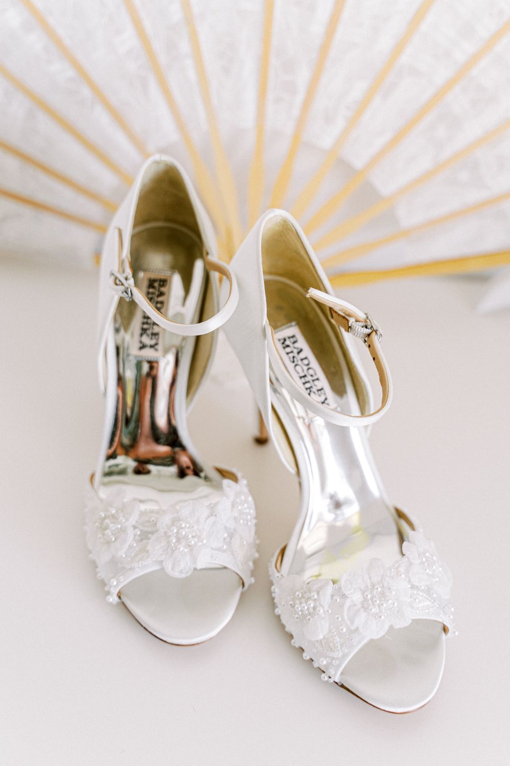 White lace embellished bridal heels arranged artistically with sunburst lighting effect in background.
