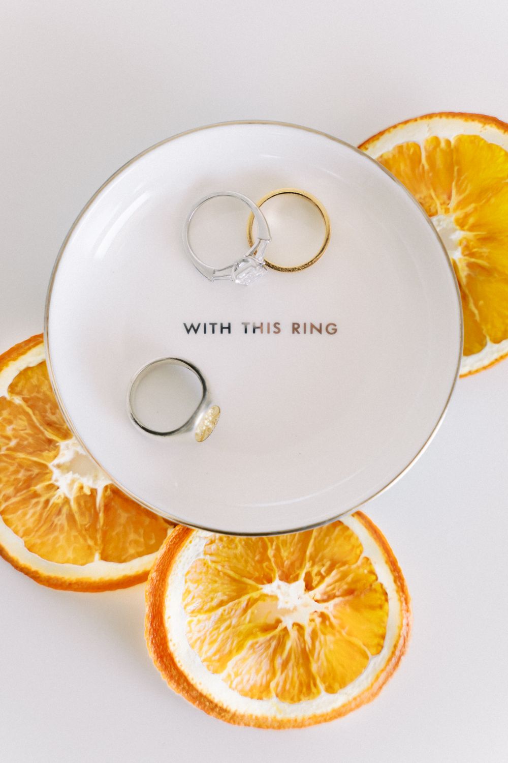 Wedding rings placed on white plates with dried orange slices creating an elegant detail shot.