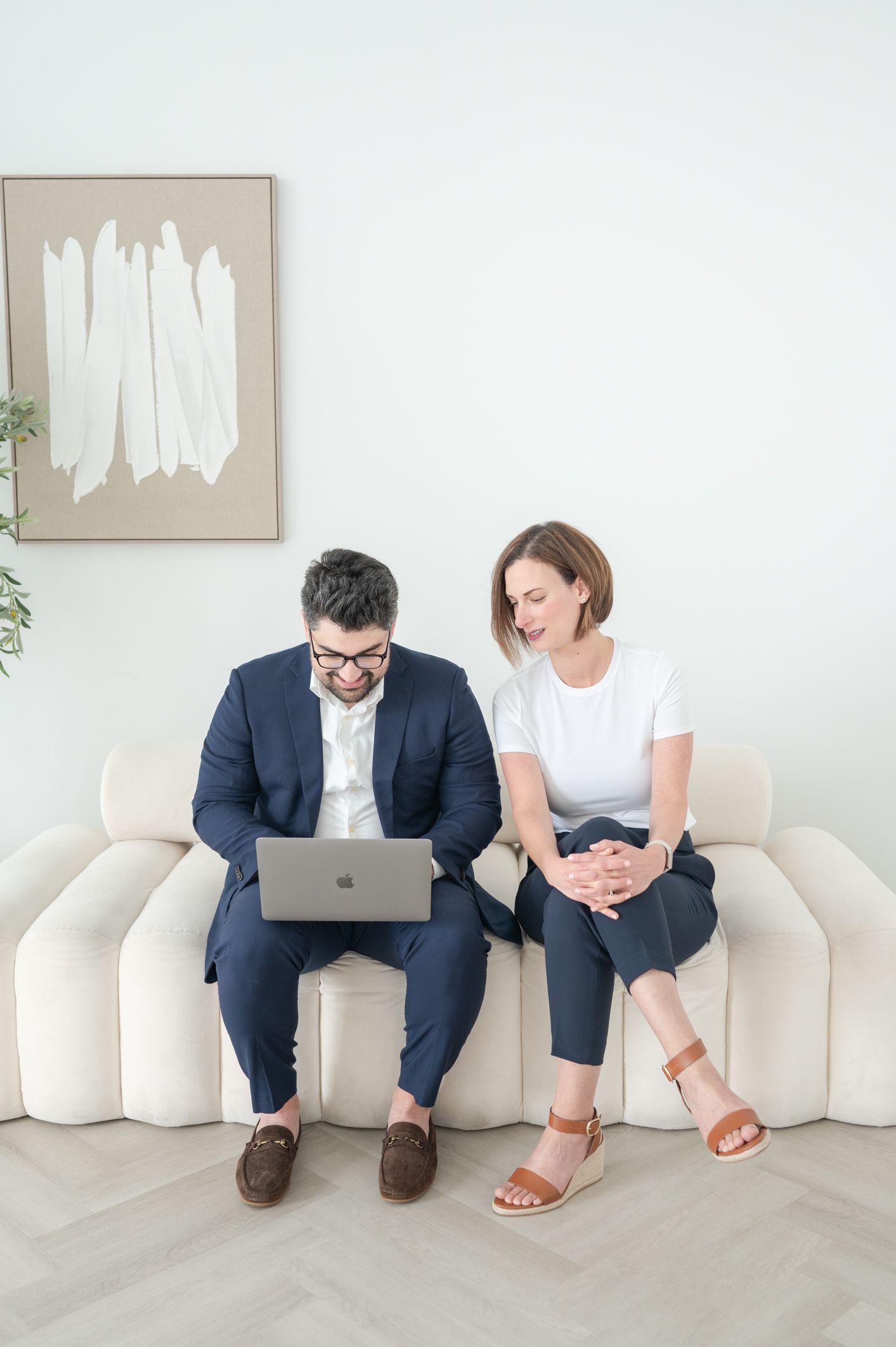 Two people sitting together on white couch in modern minimalist room with artwork.