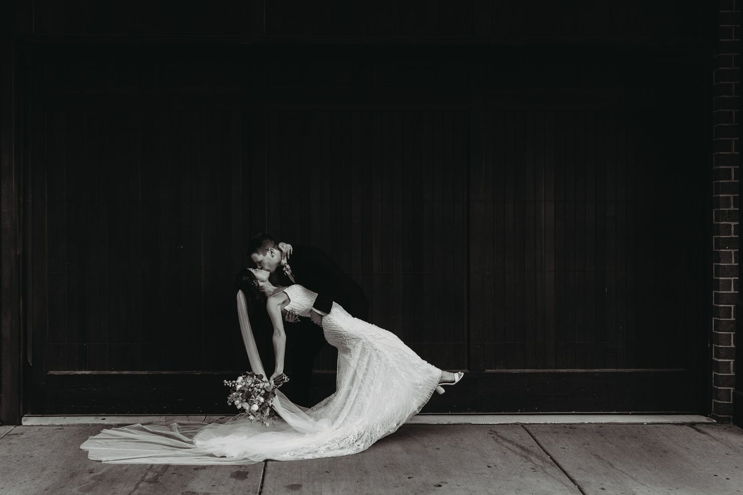 Black and white artistic photo of a dancer in a flowing white dress leaning back dramatically against a dark wall.