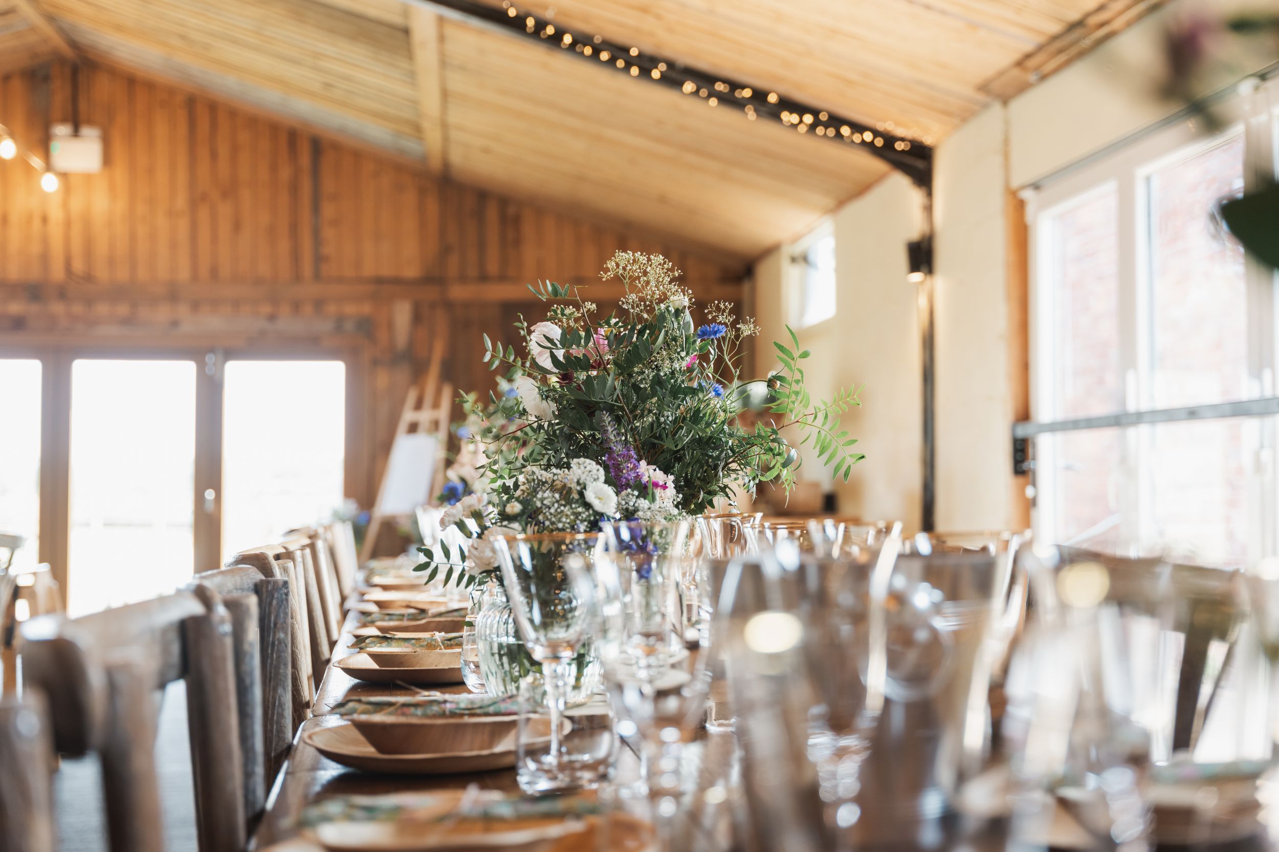 A panoramic view of a rustic wooden reception hall with long tables set for a formal dining event.