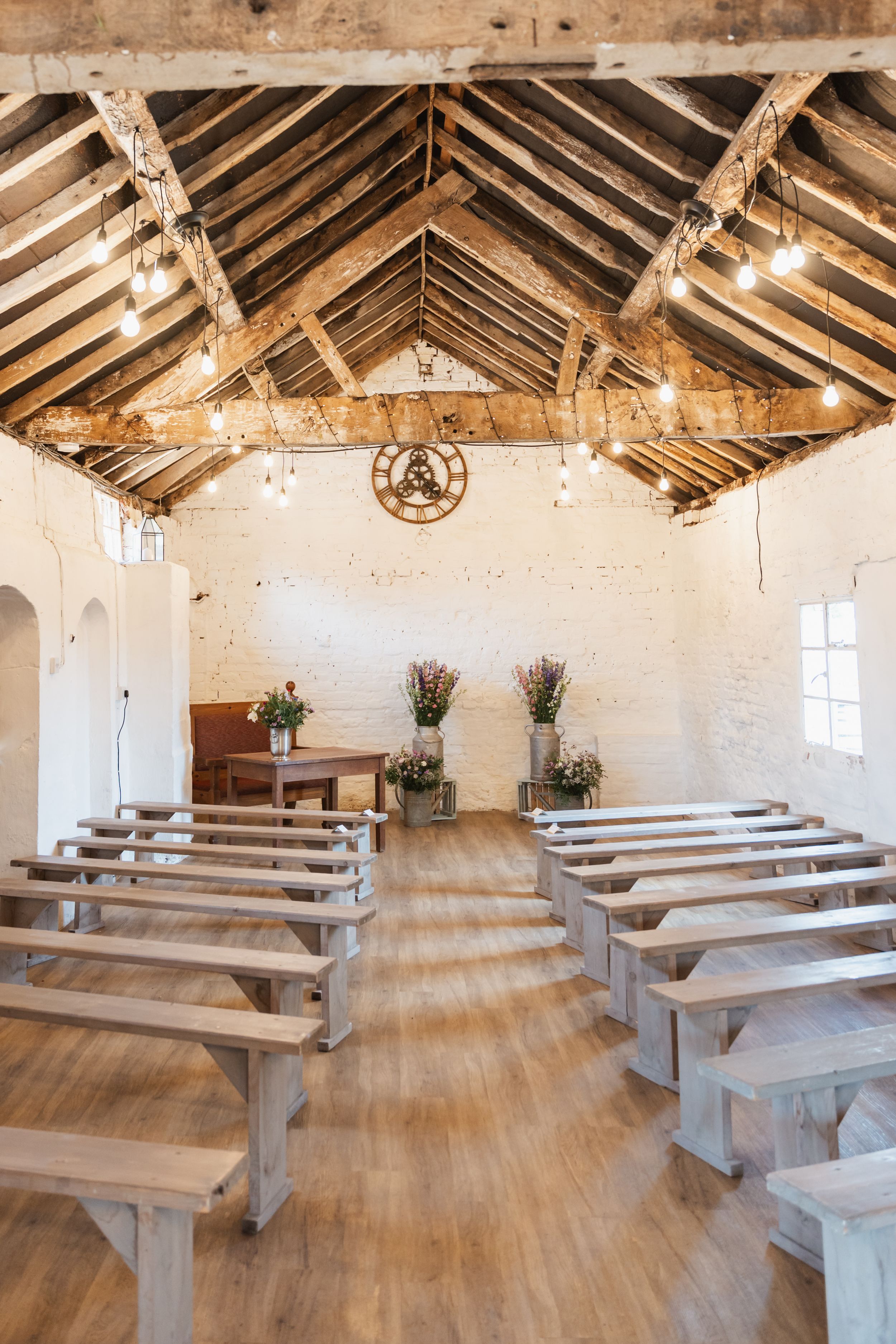 Rustic wedding chapel interior with exposed wooden beams, string lights and wooden bench seating arranged in rows.