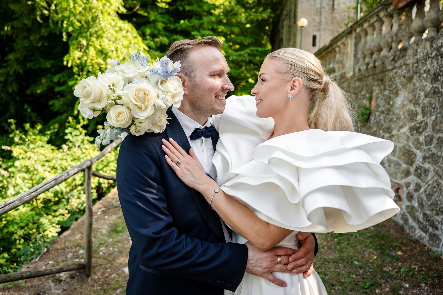 A black and white wedding photo of a couple against a stone wall with a flowing wedding dress.