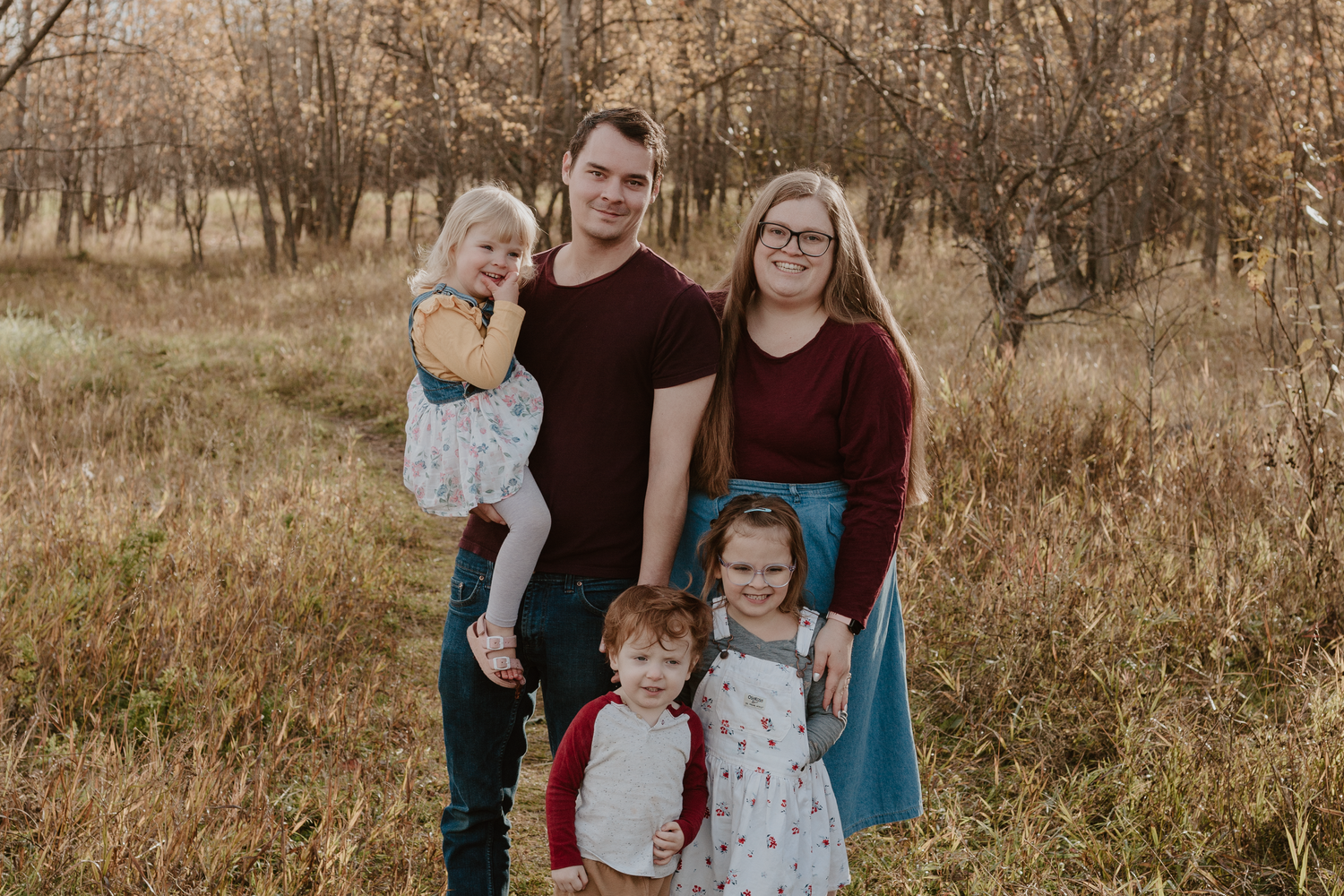 Family of five standing in a field smiling at the camera.