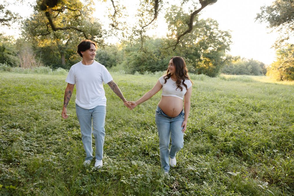 Couple walking hand in hand through a scenic meadow at sunset.