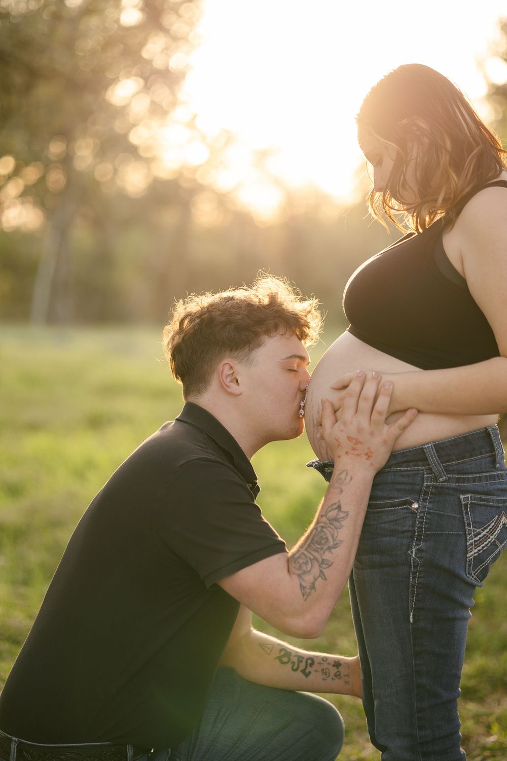 A tender maternity photoshoot sequence showing a person kissing a pregnant belly at sunset in a grassy field.