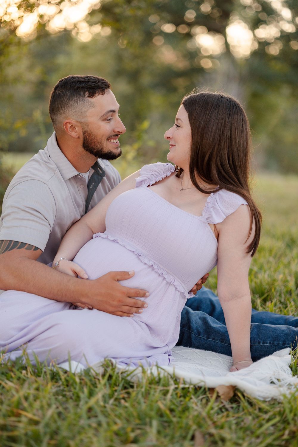 A couple shares an intimate moment outdoors during a maternity photoshoot at sunset with bokeh lighting effects.