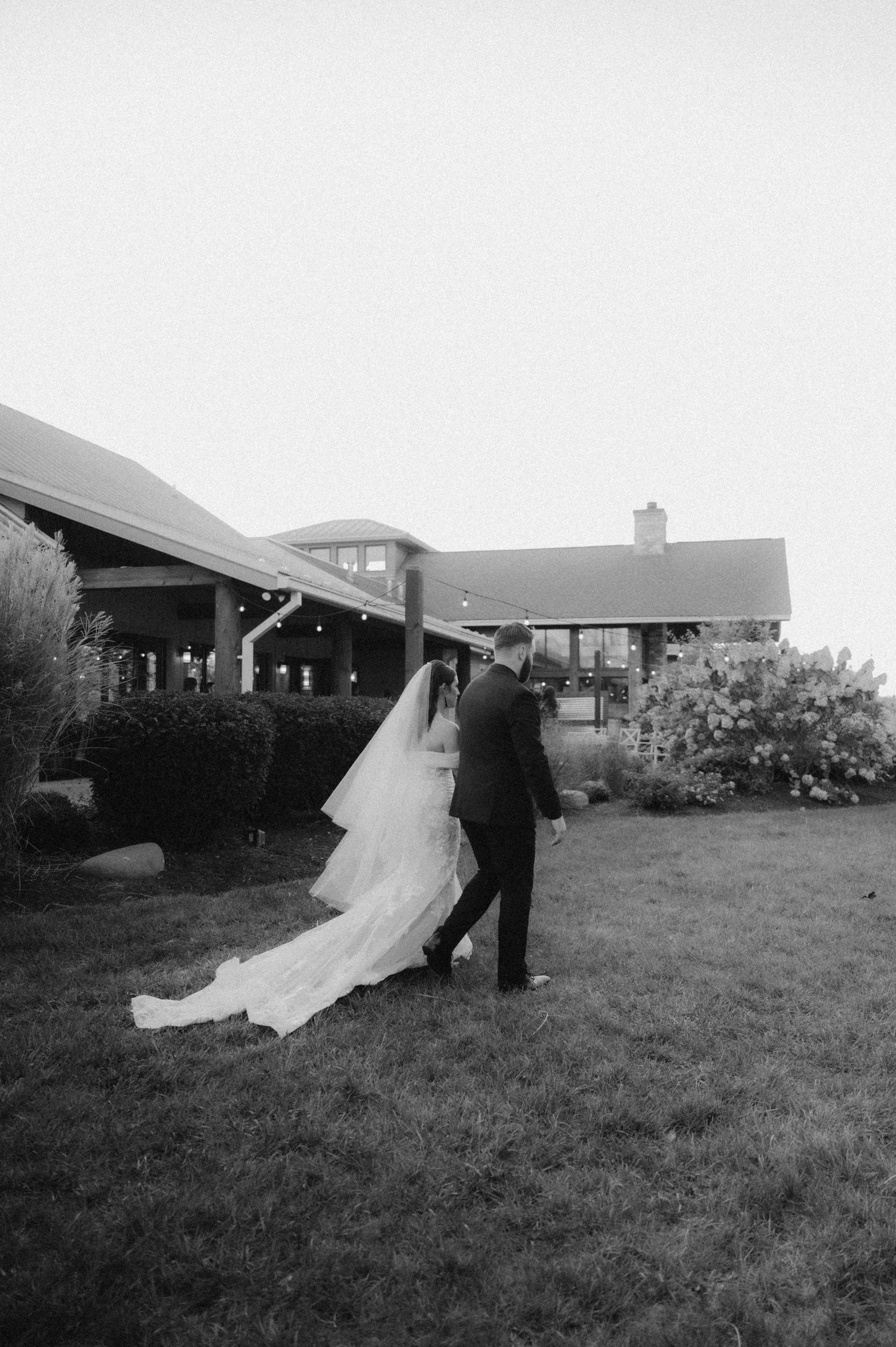Indiana Wedding and Elopement Photographer // A couple walks across a lawn in wedding attire with a flowing white dress trailing behind.