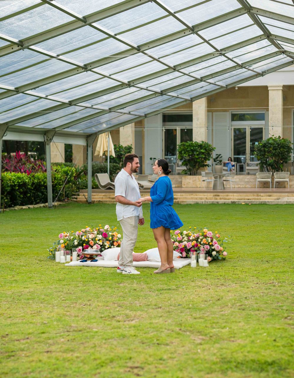 Two people share a special moment in a greenhouse surrounded by flowers and lanterns.