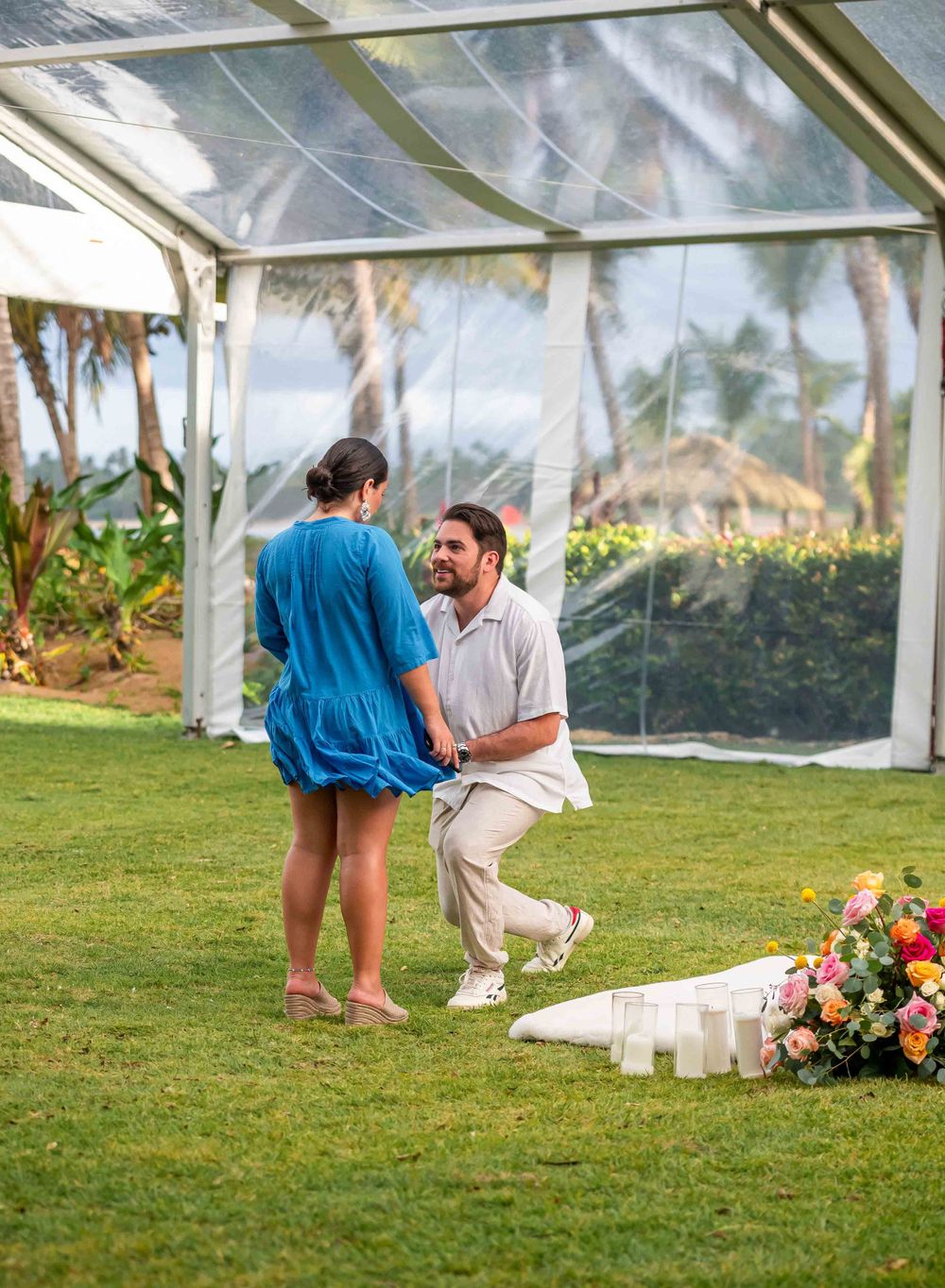 A romantic marriage proposal scene with floral decorations and candles on a grass floor.