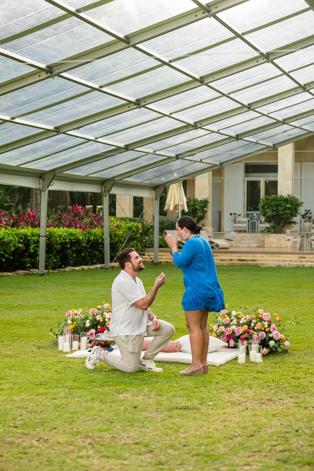 A proposal setting with floral arrangements and lanterns under a glass-covered garden structure.