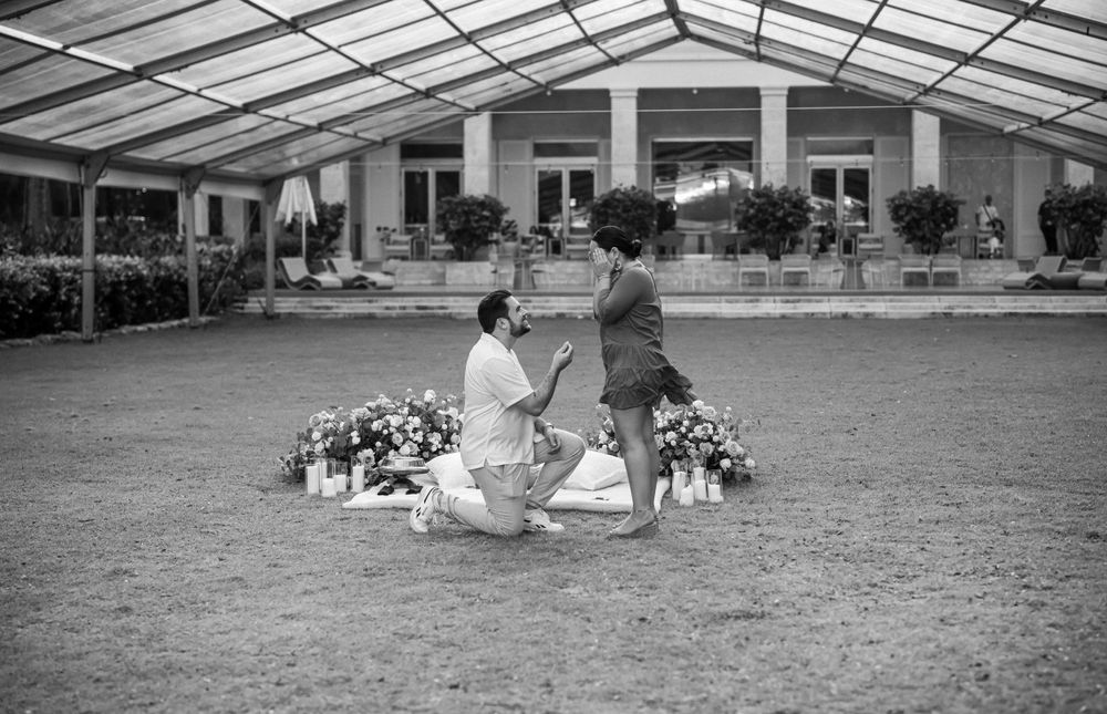 A romantic proposal moment captured in black and white with flowers decorating the outdoor venue.