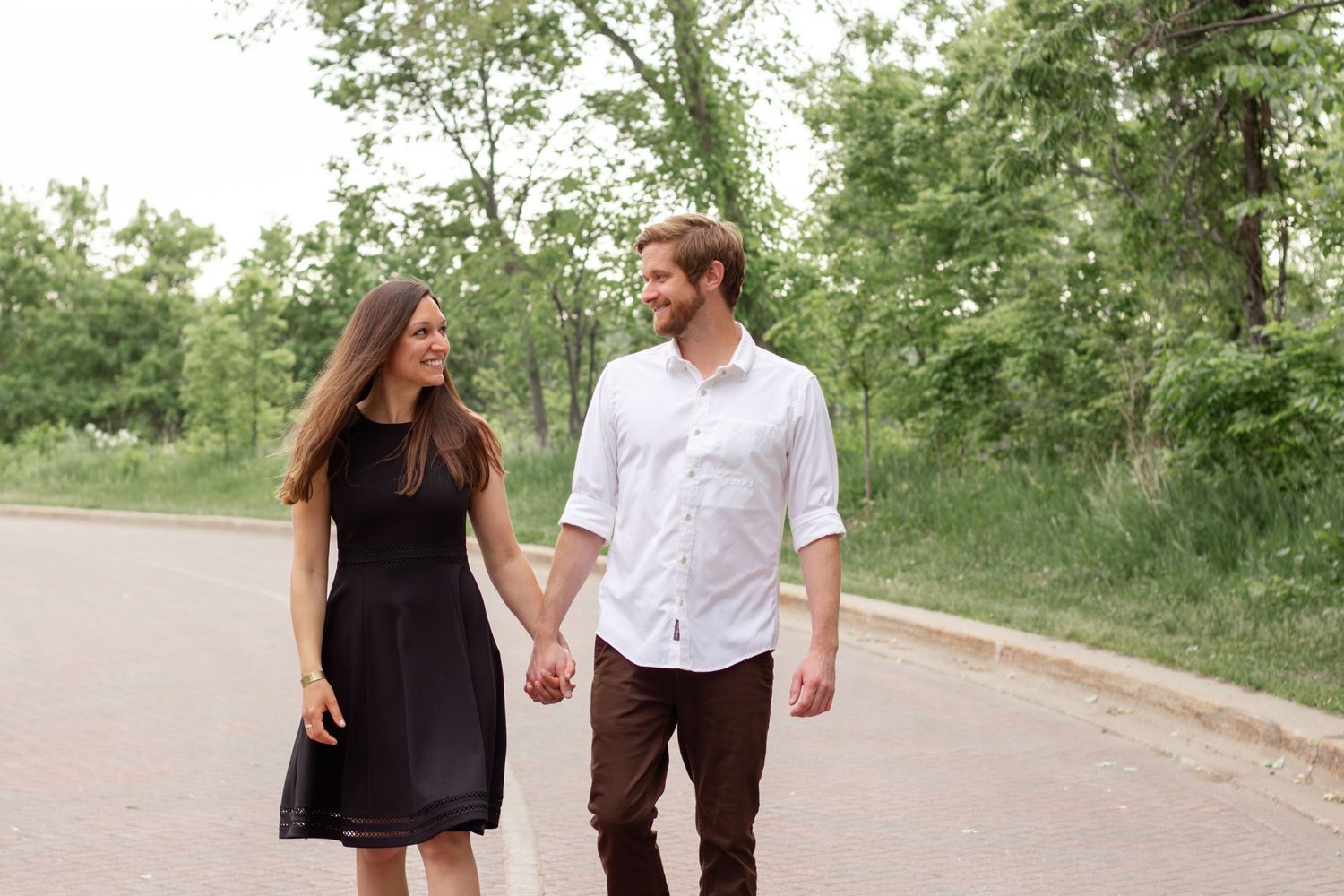 A couple walks hand in hand along a scenic tree-lined path on a sunny day.